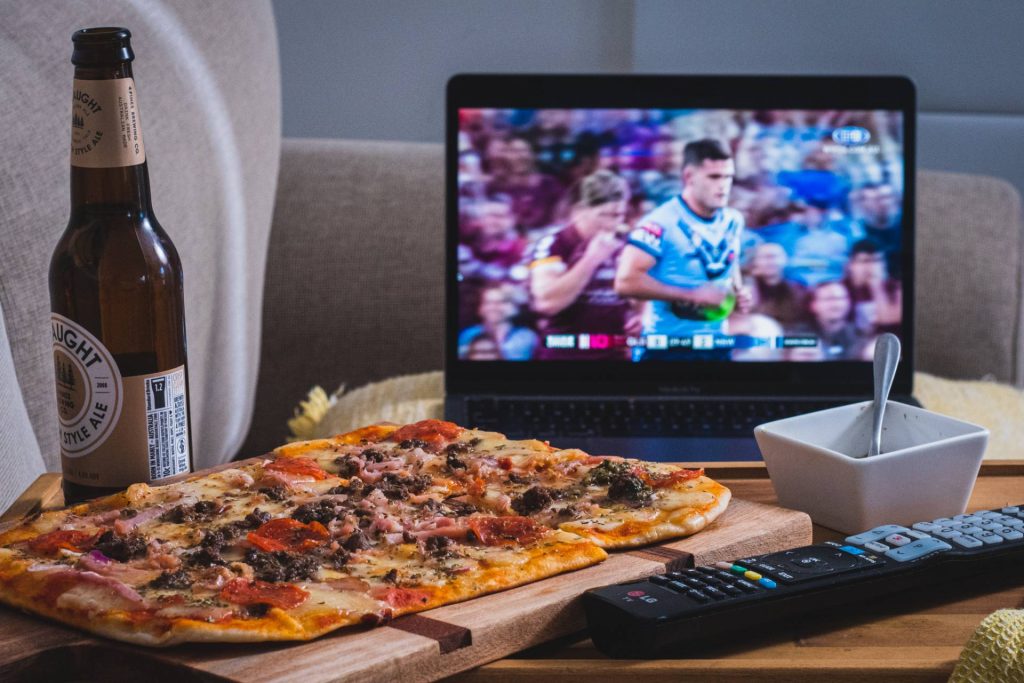 Enjoying a cold beer and wood-fired meat lovers pizza during a footy game event in Gold Coast